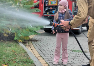 Dziecko wraz z strażakiem leje wodę w prądownicy.
