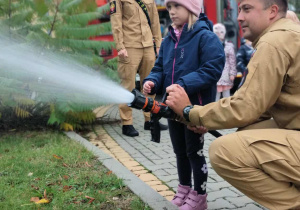 Dziecko wraz z strażakiem leje wodę w prądownicy.