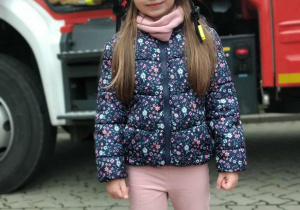 Dziecko w kasku strażackim na tle samochodu strażackiego.