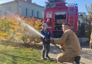 Dziecko leje wodę z węża strażackiego.