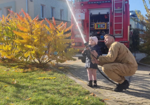 Dziecko leje wodę z węża strażackiego.