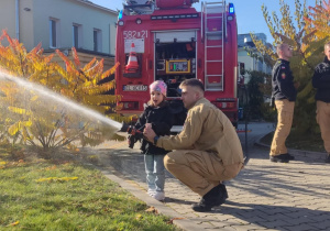 Dziecko leje wodę z węża strażackiego.