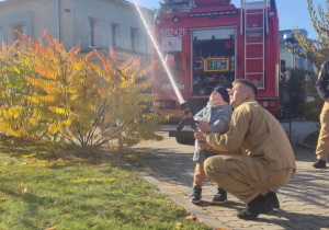 Dziecko leje wodę z węża strażackiego.