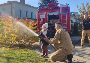 Dziecko leje wodę z węża strażackiego.