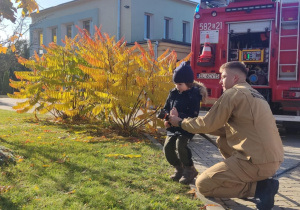 Dziecko leje wodę z węża strażackiego.