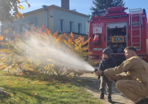 Dziecko leje wodę z węża strażackiego.