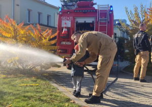 Dziecko leje wodę z węża strażackiego.