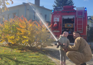 Dziecko leje wodę z węża strażackiego.