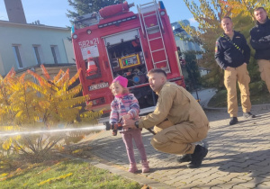 Dziecko leje wodę z węża strażackiego.
