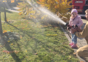 Dziecko leje wodę z węża strażackiego.