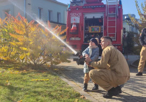 Dziecko leje wodę z węża strażackiego.