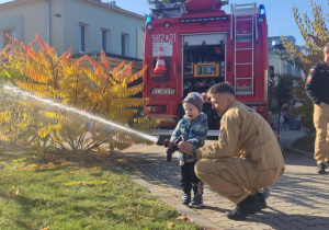 Dziecko leje wodę z węża strażackiego.