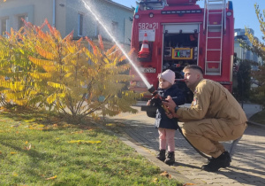Dziecko leje wodę z węża strażackiego.
