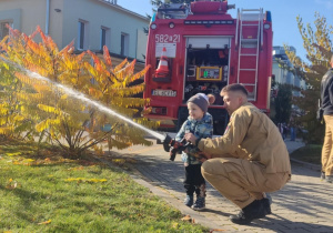 Dziecko leje wodę z węża strażackiego.
