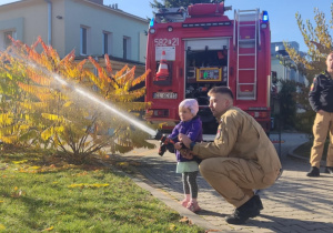 Dziecko leje wodę z węża strażackiego.