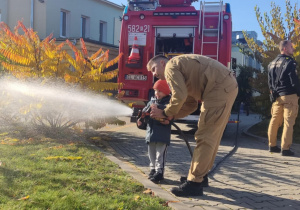 Dziecko leje wodę z węża strażackiego.