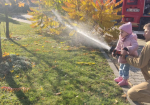 Dziecko leje wodę z węża strażackiego.