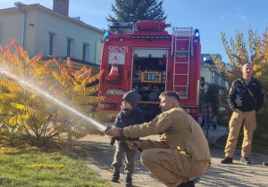 Dziecko leje wodę z węża strażackiego.
