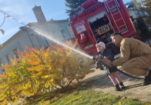 Dziecko leje wodę z węża strażackiego.