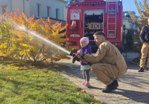 Dziecko leje wodę z węża strażackiego.
