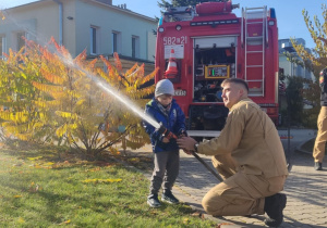 Dziecko leje wodę z węża strażackiego.