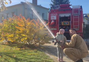 Dziecko leje wodę z węża strażackiego.