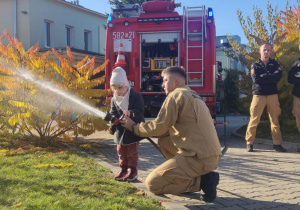 Dziecko leje wodę z węża strażackiego.