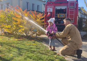 Dziecko leje wodę z węża strażackiego.