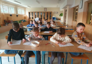 Dzieci w bibliotece przy stolikach kolorują obrazki.