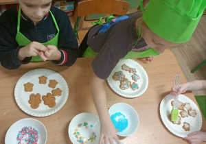 Dzieci w zielonych ubrankach dekorują pierniki.