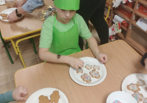 Dzieci w zielonych ubrankach dekorują pierniki.