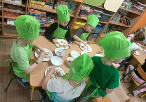 Dzieci w zielonych ubrankach dekorują pierniki.