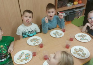 Dzieci w zielonych ubrankach dekorują pierniki.