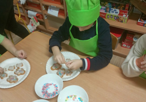 Dzieci w zielonych ubrankach dekorują pierniki.