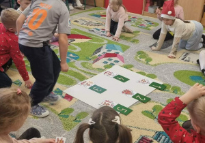 Dzieci siedzą na dywanie podczas zajęć otwartych.