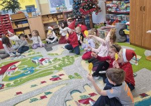 Dzieci siedzą na dywanie podczas zajęć otwartych z emotkami w rękach.