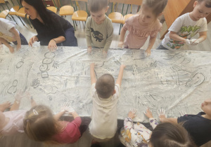 Dzieci przy stoliku malują rączkami w białej farbie.