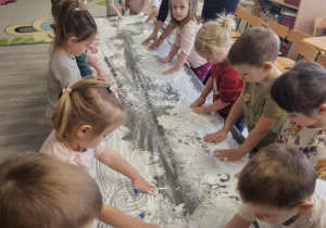 Dzieci przy stoliku malują rączkami w białej farbie.