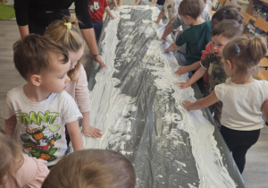 Dzieci przy stoliku malują rączkami w białej farbie.