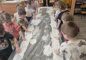 Dzieci przy stoliku malują rączkami w białej farbie.