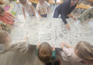 Dzieci przy stoliku malują rączkami w białej farbie.