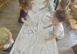 Dzieci przy stoliku malują rączkami w białej farbie.