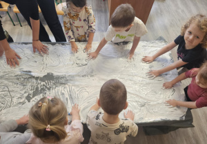 Dzieci przy stoliku malują rączkami w białej farbie.