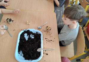 Dzieci sadzą cebulki w doniczkach.