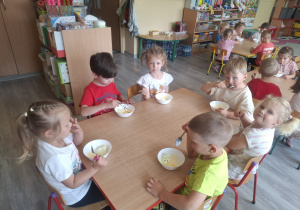 Dzieci jedzą lody przy stolikach.