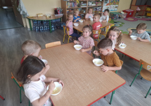 Dzieci jedzą lody przy stolikach.