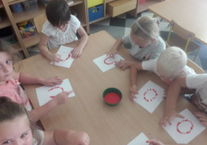 Dzieci ćwiczą kształt litery O na kartonie.