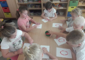 Dzieci ćwiczą kształt litery O na kartonie.