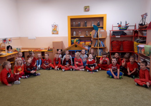 Dzieci ubrane na czerwono, siedzą na dywanie. Dzień czerwony w przedszkolu.