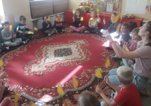 Dzieci siedzą w kole, na dywanie.